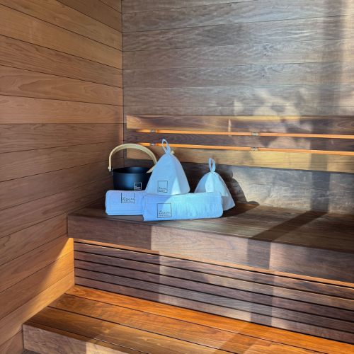 Muskoka Sauna interior with traditional Finnish sauna accessories including wooden bucket, ladle, and felt hat on cedar bench with modern LED accent lighting.