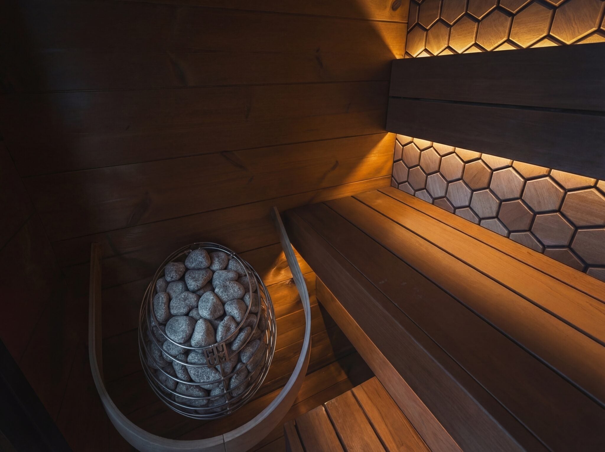 Wooden sauna interior with a basket of stones and hexagonal tile pattern.